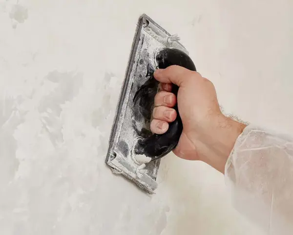 Main d'artisan ponçant un mur pour un fini lisse en béton ciré.