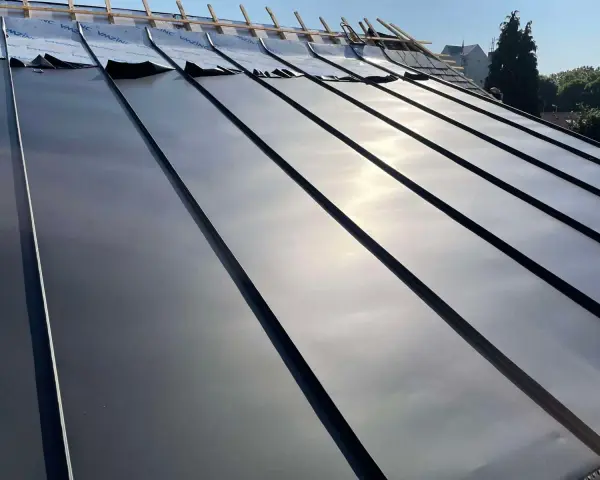 Pose de feuilles de toit en zinc sur une nouvelle construction. Le soleil brille sur le métal lisse.