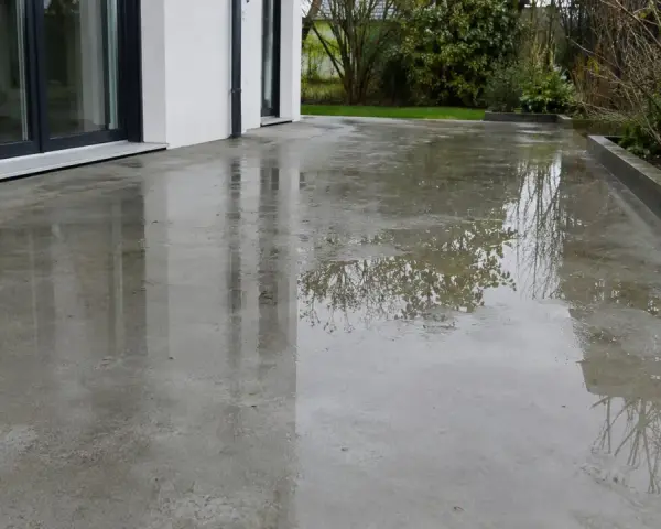 Surface de béton mouillée reflétant le ciel et les arbres. Une **infiltration terrasse** est visible, avec des flaques d'eau sur le sol.
