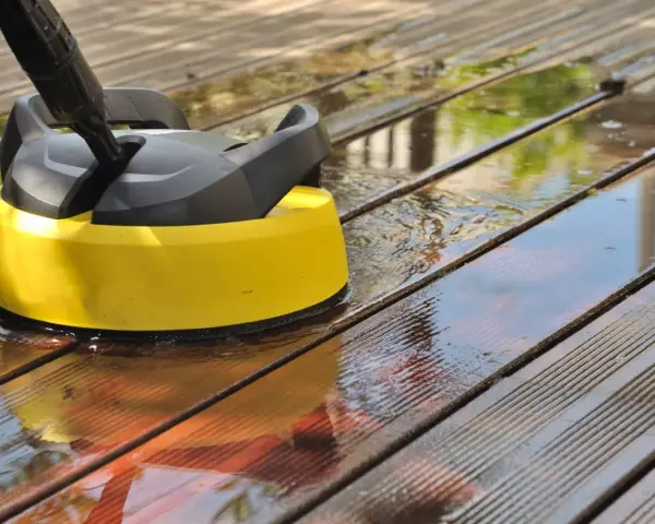 Nettoyer une terrasse en composite avec un nettoyeur haute pression. L'eau éclabousse sur les lattes de bois.