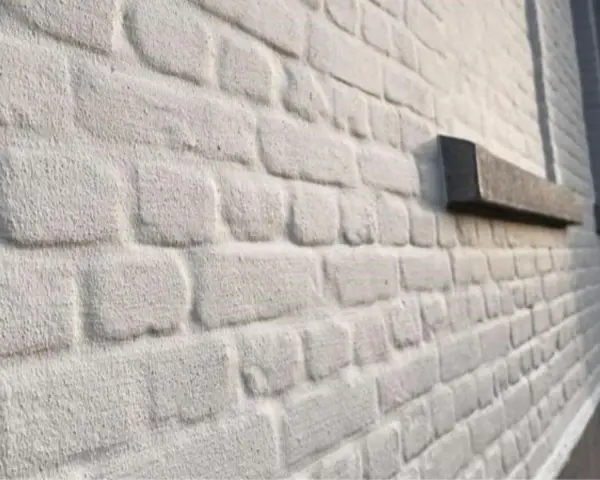 Mur en briques blanchies au badigeon à la chaux, avec un rebord de fenêtre en pierre sombre.