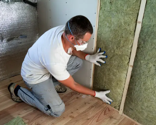 Un ouvrier installe de la laine de verre inflammable dans un mur, portant masque et lunettes de protection.
