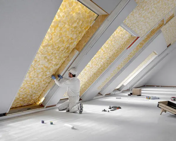 Un ouvrier installe un isolant thermique jaune texturé dans un grenier. C'est le meilleur isolant thermique pour une maison confortable.