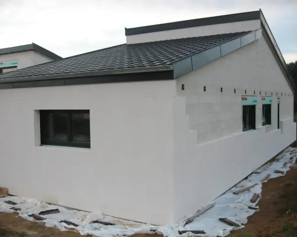 Maison en construction avec murs en **béton cellulaire extérieur**. Fenêtres noires et toit sombre.