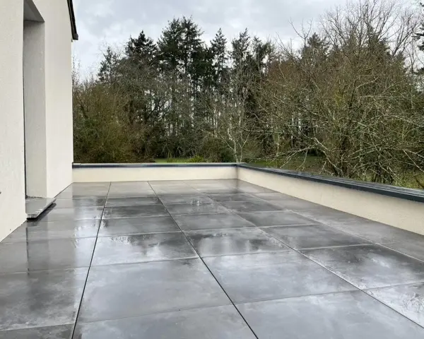 Terrasse avec dalles grises sur un toit plat, offrant une vue sur une forêt. L'étanchéité du toit plat est assurée pour une durabilité optimale.