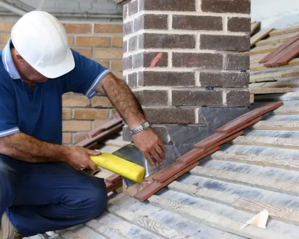 Un couvreur installe un solin en plomb pour l'étanchéité de cheminée, assurant une protection durable contre les intempéries.