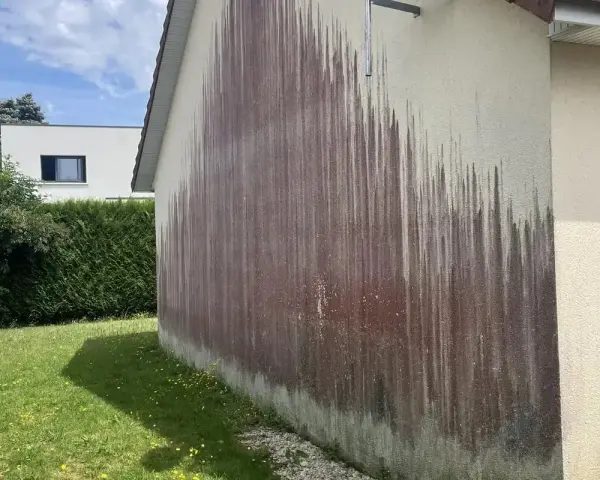 Traces sombres sur un mur extérieur, probablement dues à des algues rouges et à l'eau de javel.