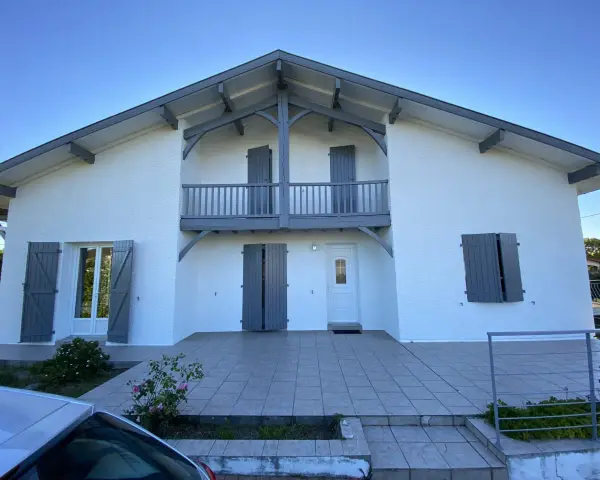 La façade maison 2 couleurs, blanche et grise, présente un balcon avec des volets assortis.