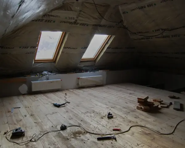 Grenier en cours d'aménagement, avec pare-vapeur fibre de bois, deux fenêtres de toit et un plancher en bois brut. Outils de bricolage au sol.