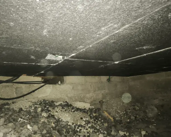 Vue de dessous d'un plancher, montrant le matériau d'isolation du plancher bas, des tuyaux et des blocs de béton.