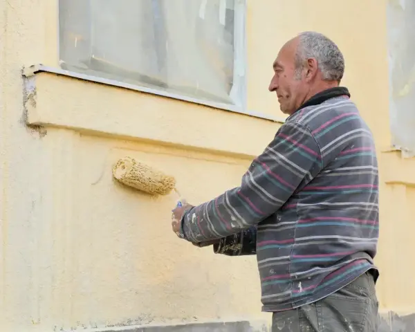 Un homme peint une façade jaune avec un rouleau.
