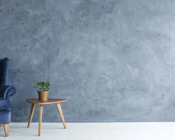 Fauteuil bleu profond devant un mur texturé avec une peinture effet stucco. Une petite table en bois supporte une plante verte.