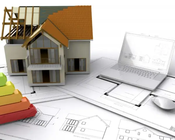 Maquette de maison, échelle d'énergie, plans et ordinateur portable. L'isolation RGE Qualibat est essentielle pour une maison performante.