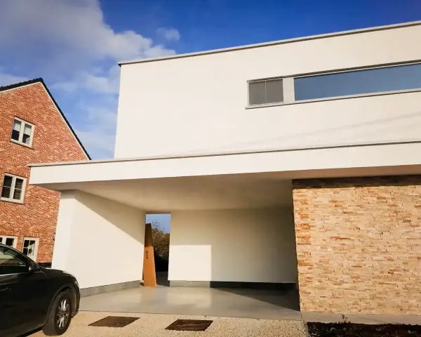 Maison moderne avec façade en crépi blanc immaculé, prête pour un nettoyage. Une voiture noire est garée sous l'auvent.