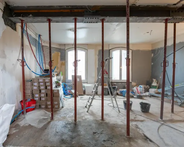Chantiers : étais métalliques soutenant une poutre en cours de consolidation pour le prix d'une fondation maison. Matériaux et outils de construction visibles.