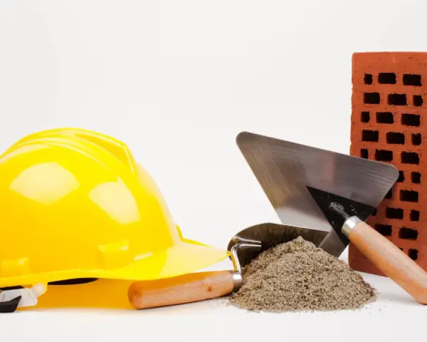 Casque jaune, brique rouge, tas de sable et truelles : les outils maçon essentiels pour bâtir.