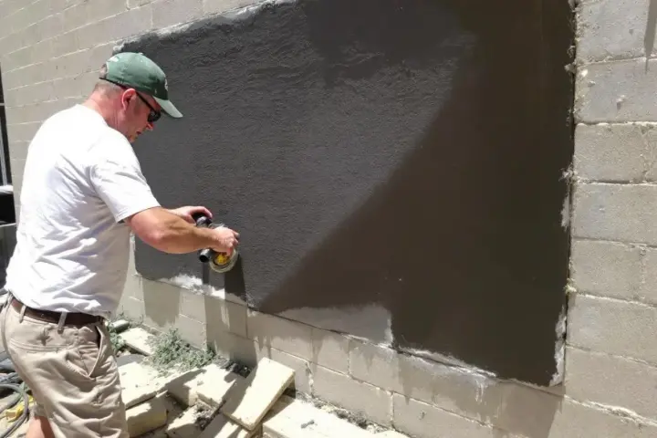 Un homme utilise une ponceuse pour araser un mur extérieur fraîchement enduit.