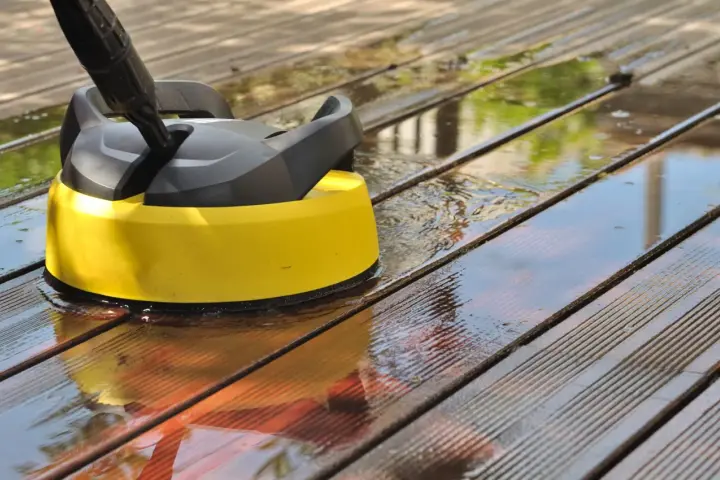 Nettoyer une terrasse en composite avec un nettoyeur haute pression. L'eau éclabousse sur les lattes de bois.