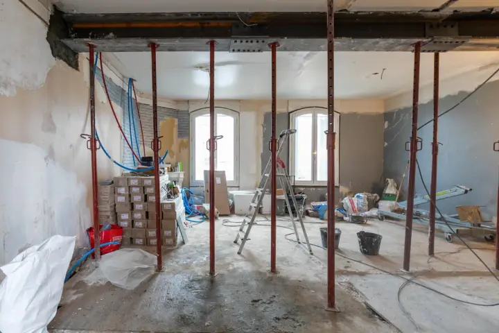 Chantiers : étais métalliques soutenant une poutre en cours de consolidation pour le prix d'une fondation maison. Matériaux et outils de construction visibles.