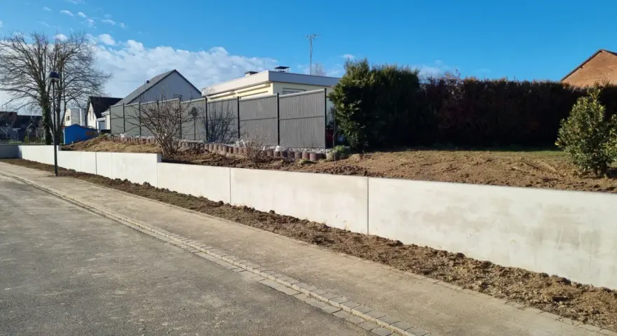 La **fondation mur de soutènement** en béton est prête pour le jardinage. Le ciel bleu et les maisons en arrière-plan annoncent le printemps.