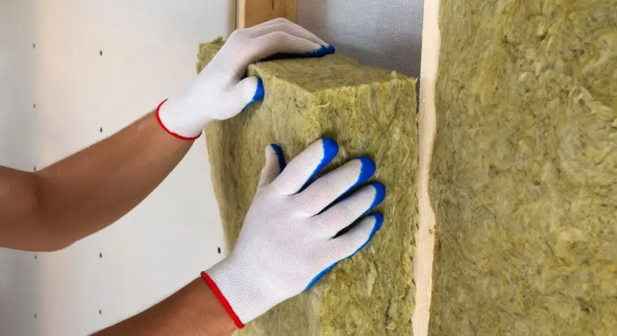 Pose d'isolant en laine de roche dans un mur. Les mains gantées ajustent le matériau pour une isolation optimale.