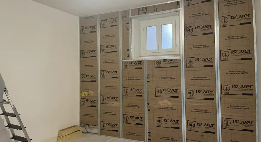 Pose de laine de verre ISOVER en 2 couches sur une structure métallique, avec une fenêtre au centre.