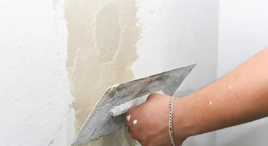 Main d'un artisan appliquant de l'enduit pour réparer une fissure crepis maison.