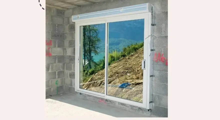 Fenêtre coulissante en PVC installée dans un mur en parpaings, offrant une vue sur un paysage montagneux. Idéal pour apprendre comment poser une fenêtre de toit.