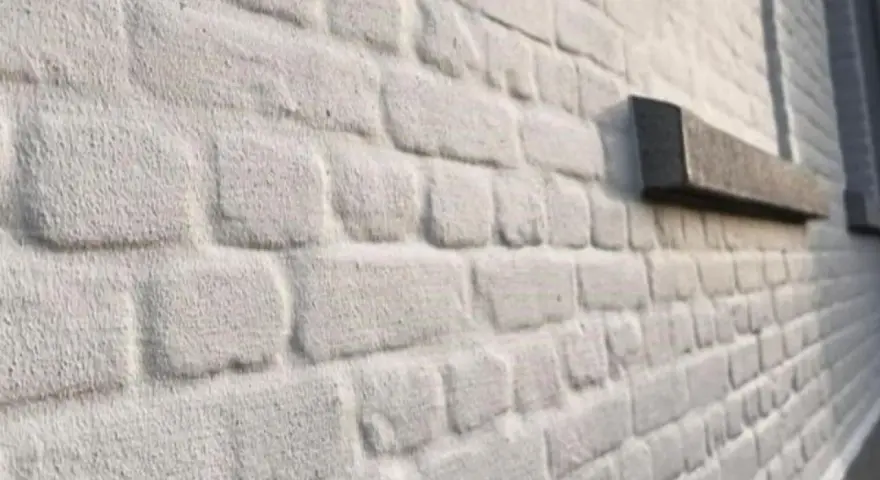 Mur en briques blanchies au badigeon à la chaux, avec un rebord de fenêtre en pierre sombre.