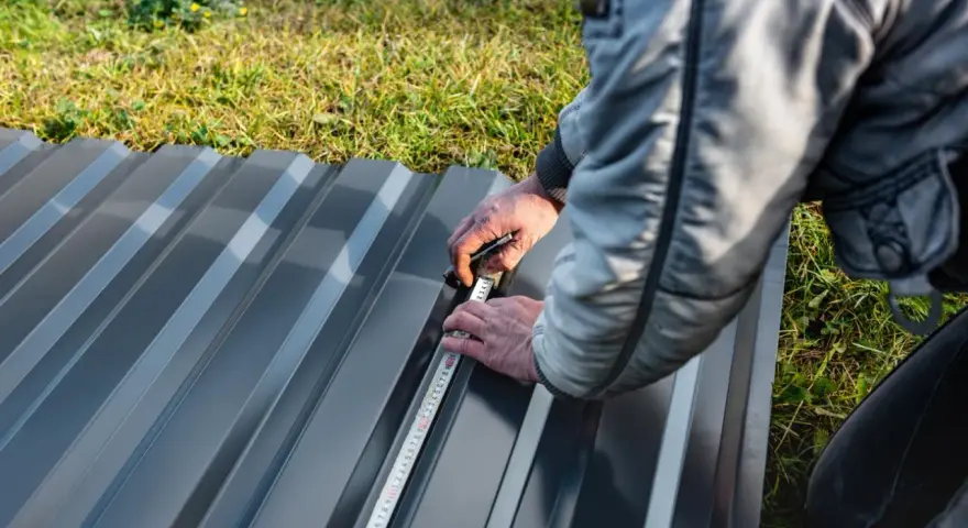 Un ouvrier mesure une tôle de bac acier pour un toit plat.