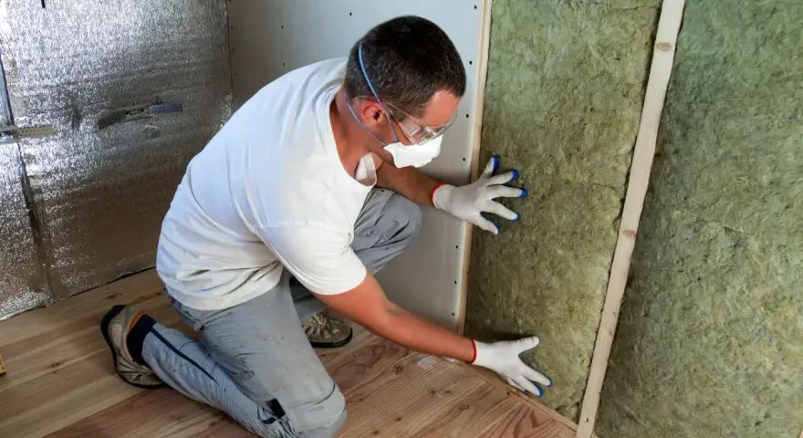 Un ouvrier installe de la laine de verre inflammable dans un mur, portant masque et lunettes de protection.