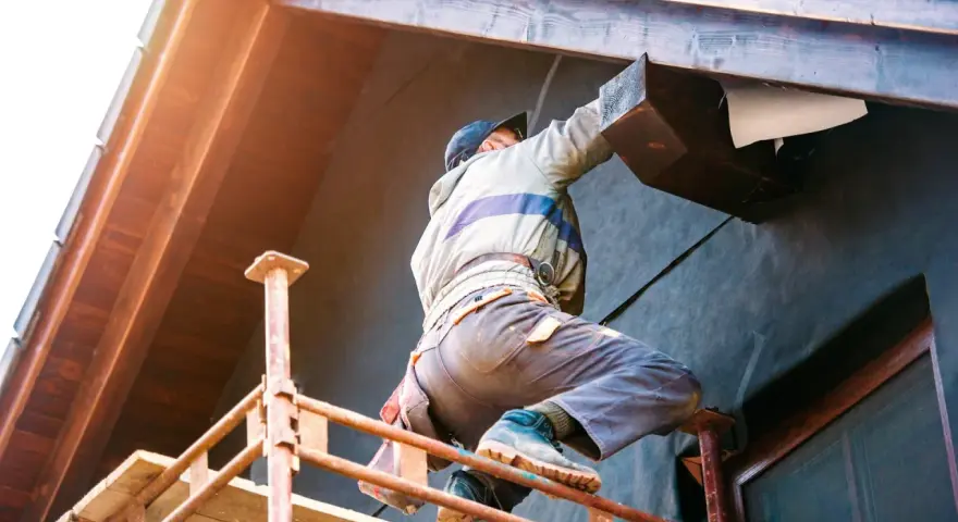 Un ouvrier sur échafaudage réalise l'isolation extérieure d'une maison. Une entreprise RGE pour des travaux d'isolation extérieure performants.