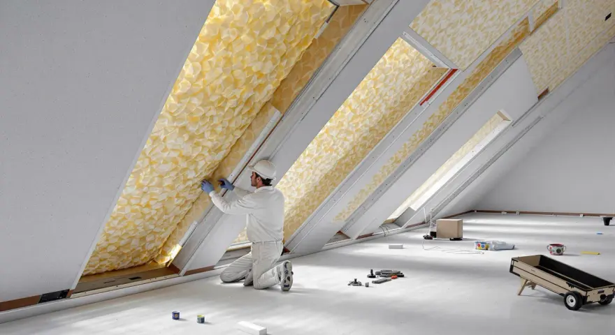 Un ouvrier installe un isolant thermique jaune texturé dans un grenier. C'est le meilleur isolant thermique pour une maison confortable.