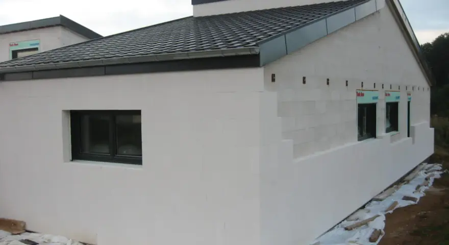 Maison en construction avec murs en **béton cellulaire extérieur**. Fenêtres noires et toit sombre.