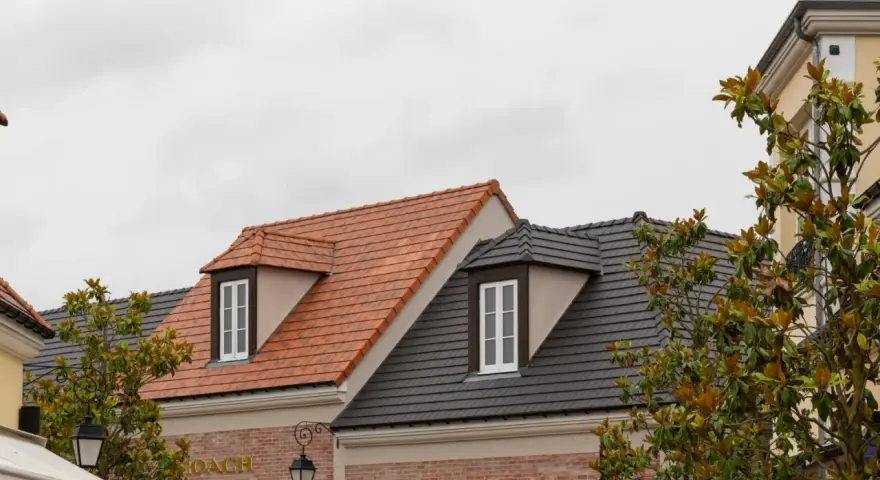 Toits de bâtiments avec différents types de tuiles : une toiture en tuiles d'argile orangées et une autre en tuiles d'ardoise grises.