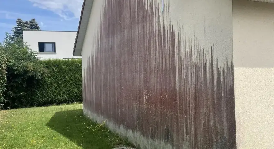 Traces sombres sur un mur extérieur, probablement dues à des algues rouges et à l'eau de javel.