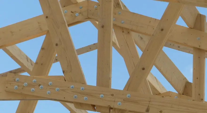 Assemblage ferme charpente en bois, structure solide sous un ciel bleu.
