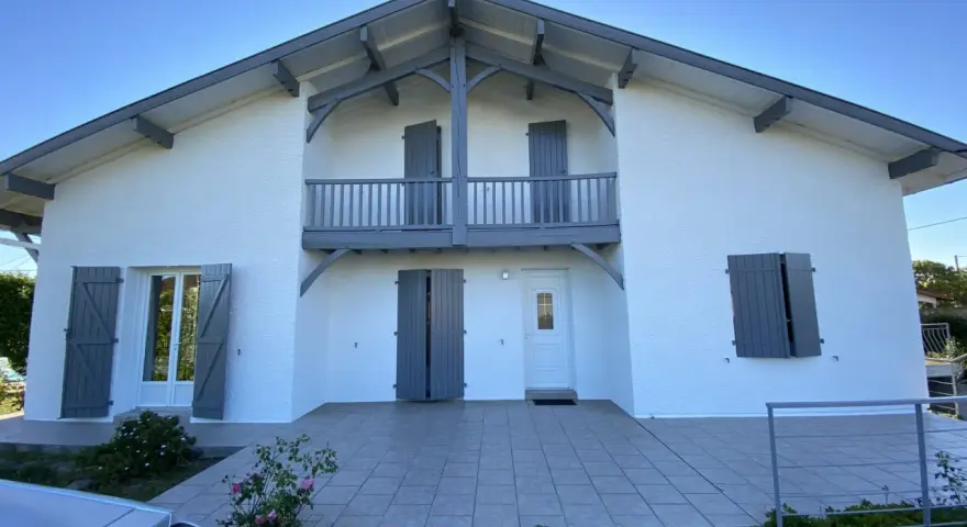 La façade maison 2 couleurs, blanche et grise, présente un balcon avec des volets assortis.