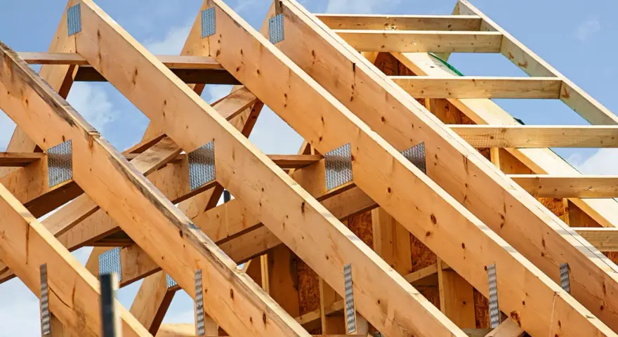 Structure en bois d'une charpente de toiture, avec des poutres assemblées par des connecteurs métalliques sous un ciel bleu.
