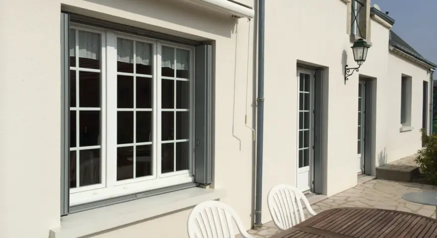 Un grand **appui de fenêtre** blanc orne la façade d'une maison. Des volets gris sont partiellement ouverts.