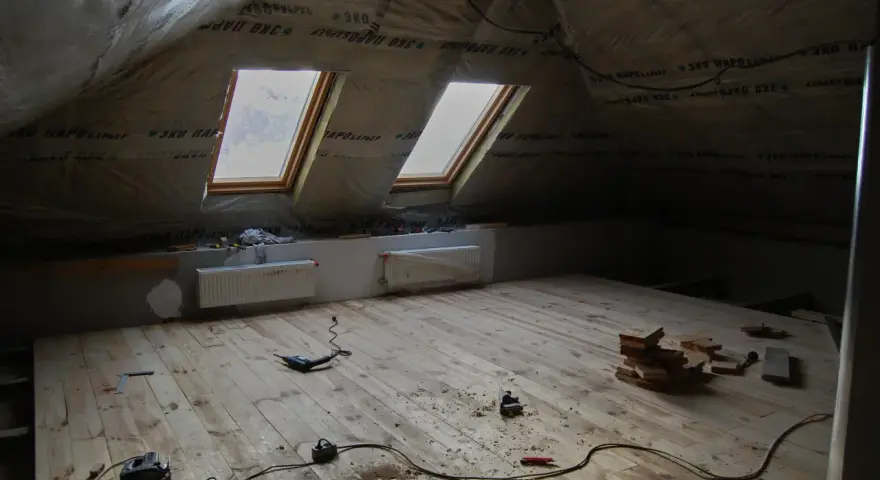 Grenier en cours d'aménagement, avec pare-vapeur fibre de bois, deux fenêtres de toit et un plancher en bois brut. Outils de bricolage au sol.