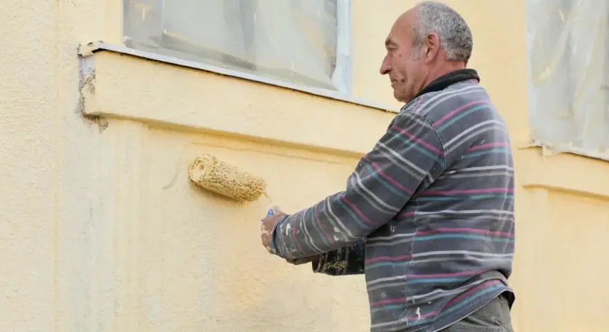 Un homme peint une façade jaune avec un rouleau.