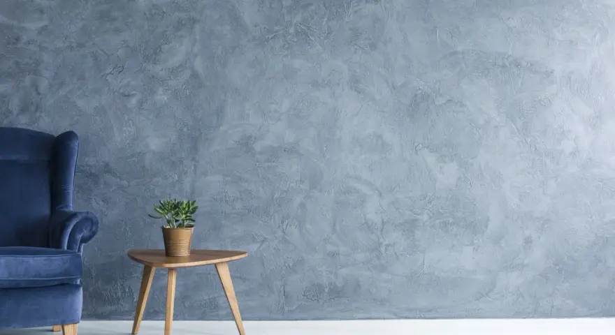 Fauteuil bleu profond devant un mur texturé avec une peinture effet stucco. Une petite table en bois supporte une plante verte.