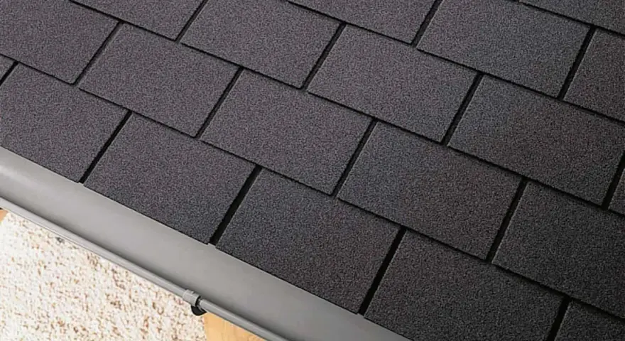 Détail d'une toiture en pose de bardeau bitumé gris foncé, avec une gouttière grise.