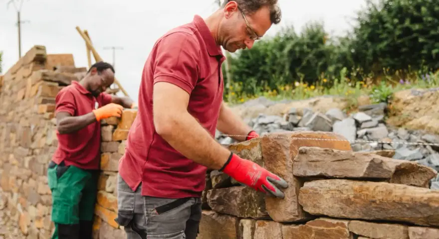 Deux maçons construisent un mur en pierre sèche.