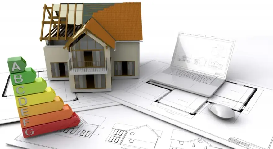 Maquette de maison, échelle d'énergie, plans et ordinateur portable. L'isolation RGE Qualibat est essentielle pour une maison performante.