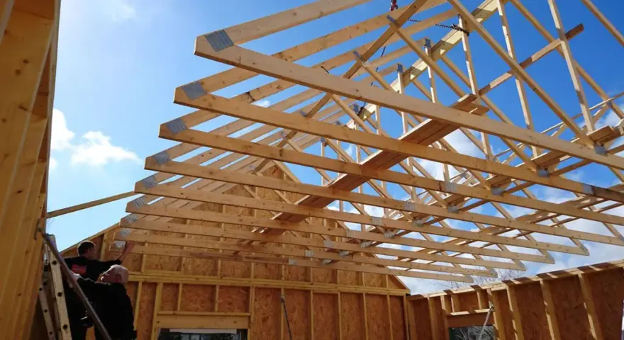 Construction d'une charpente fermette en bois sous un ciel bleu. Des ouvriers travaillent sur l'installation.