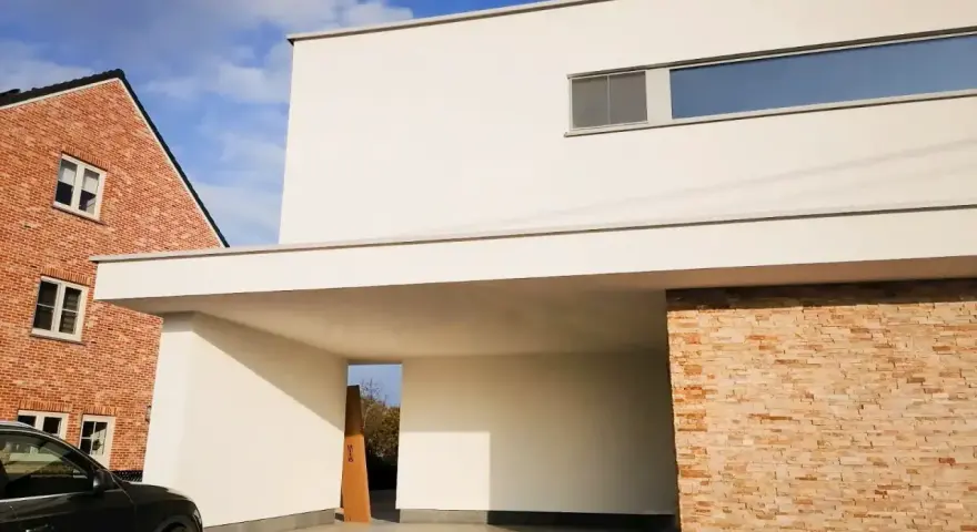 Maison moderne avec façade en crépi blanc immaculé, prête pour un nettoyage. Une voiture noire est garée sous l'auvent.