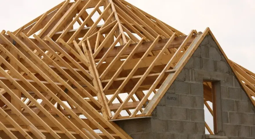 Structure en bois d'une charpente simple, en cours de construction. Les poutres de bois forment un motif complexe au-dessus des murs en blocs de béton.