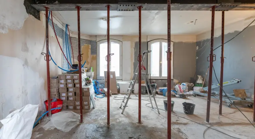 Chantiers : étais métalliques soutenant une poutre en cours de consolidation pour le prix d'une fondation maison. Matériaux et outils de construction visibles.